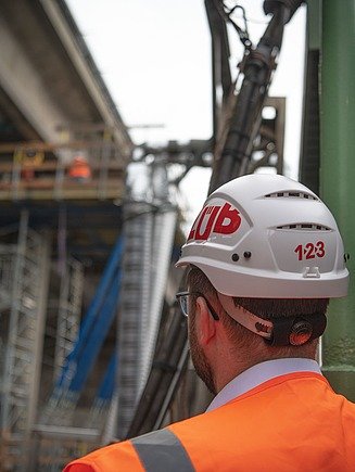 Foto einer Person von hinten mit Helm und einer Brücke im Hintergrund