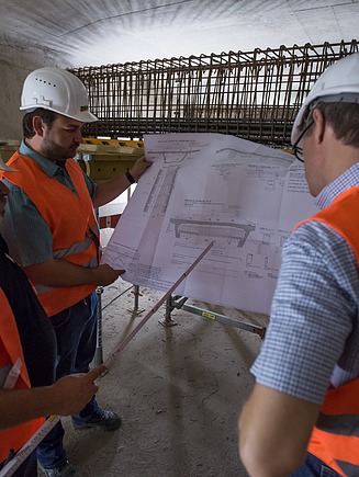 Foto von drei Personen mit Baustellenausrüstung und einem Plan in der Hand