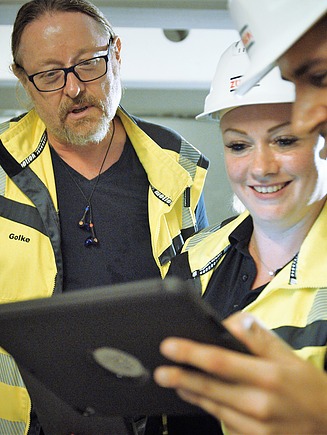 Foto von drei Personen mit Blick auf ein Tablet gerichtet