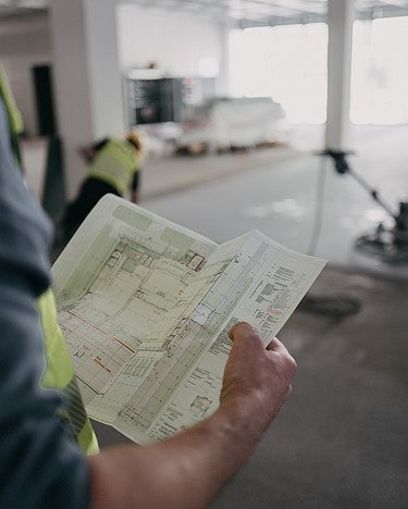 Nachwuchsingenieurprogramm bei der ZÜBLIN Bauwerkserhaltung Foto einer Person von hinten mit Blick auf einen Gebäudeplan