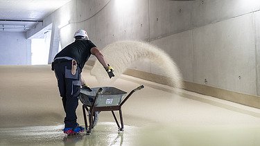 Nachbehandlung der Spezialbeschichtung Foto einer Person die auf einer frisch beschichteten Fläche steht und Körner einstreut